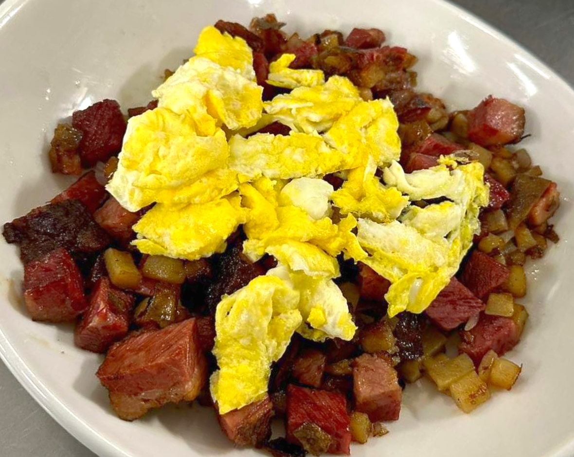 Scrambled eggs over diced potatoes and corned beef in a white bowl
