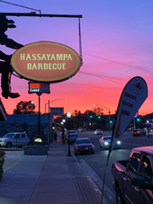 Hassayampa Barbecue sign at sunset on a city sidewalk, with cars and a purple-pink sky