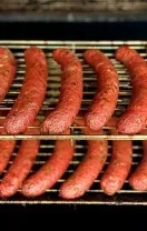 Rows of sausages grilling on a barbecue rack over glowing coals.