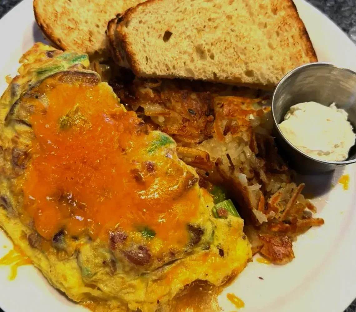 Plate of omelet with orange sauce, bread slices, shredded meat, and a small cup of butter.
