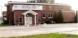 Brick building with white trim and a small covered entrance beside a road