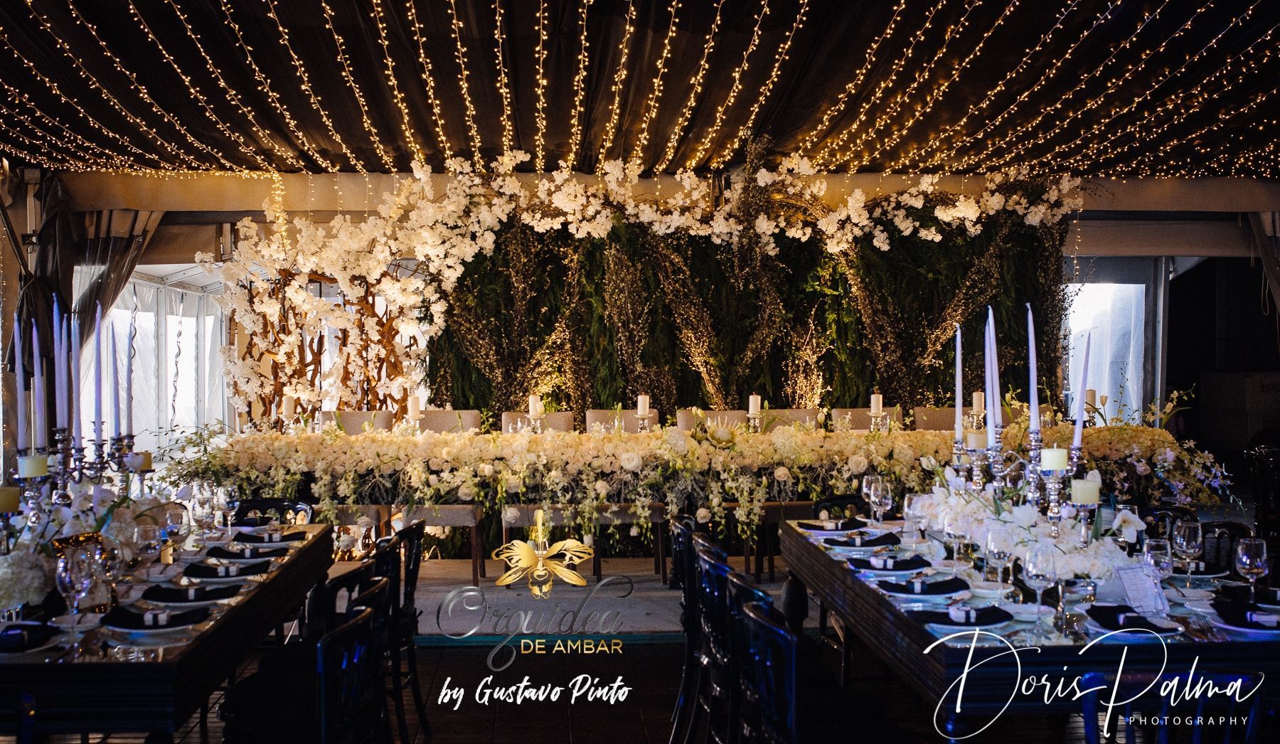 A long table with a lot of flowers and lights on the ceiling.