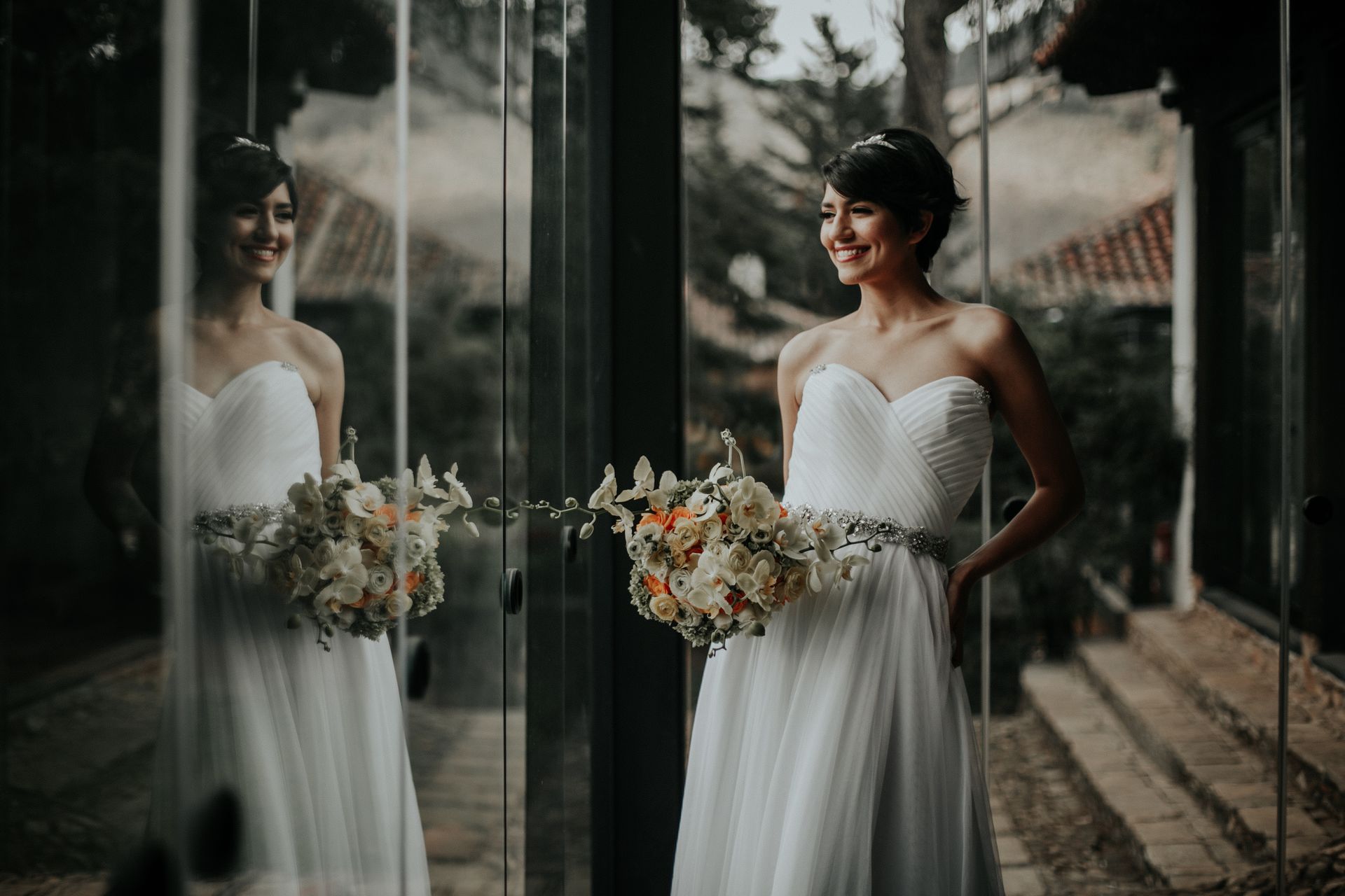 A bride in a white dress is standing in front of a mirror holding a bouquet of flowers.