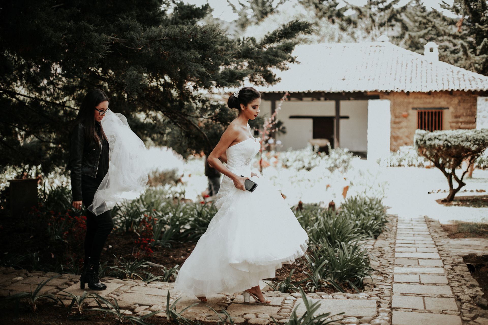 A bride and groom are walking down a path in front of a house.