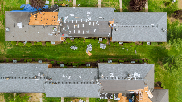 Aerial view of buildings with damaged roofs and scattered debris on the grass.