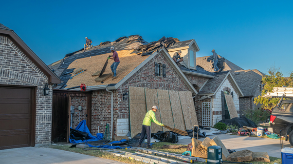 Workers repairing a damaged roof on a house, installing new wooden panels.