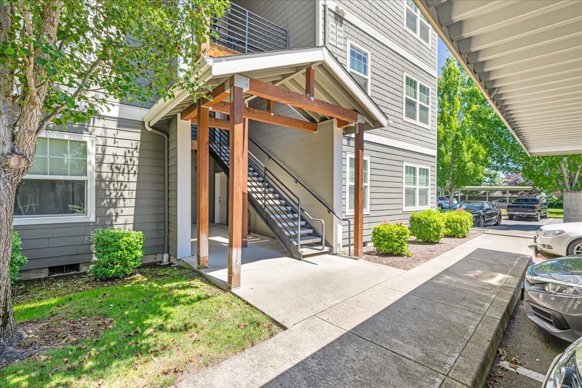 Apartment building entrance with covered stairs, landscaping, and a car park.