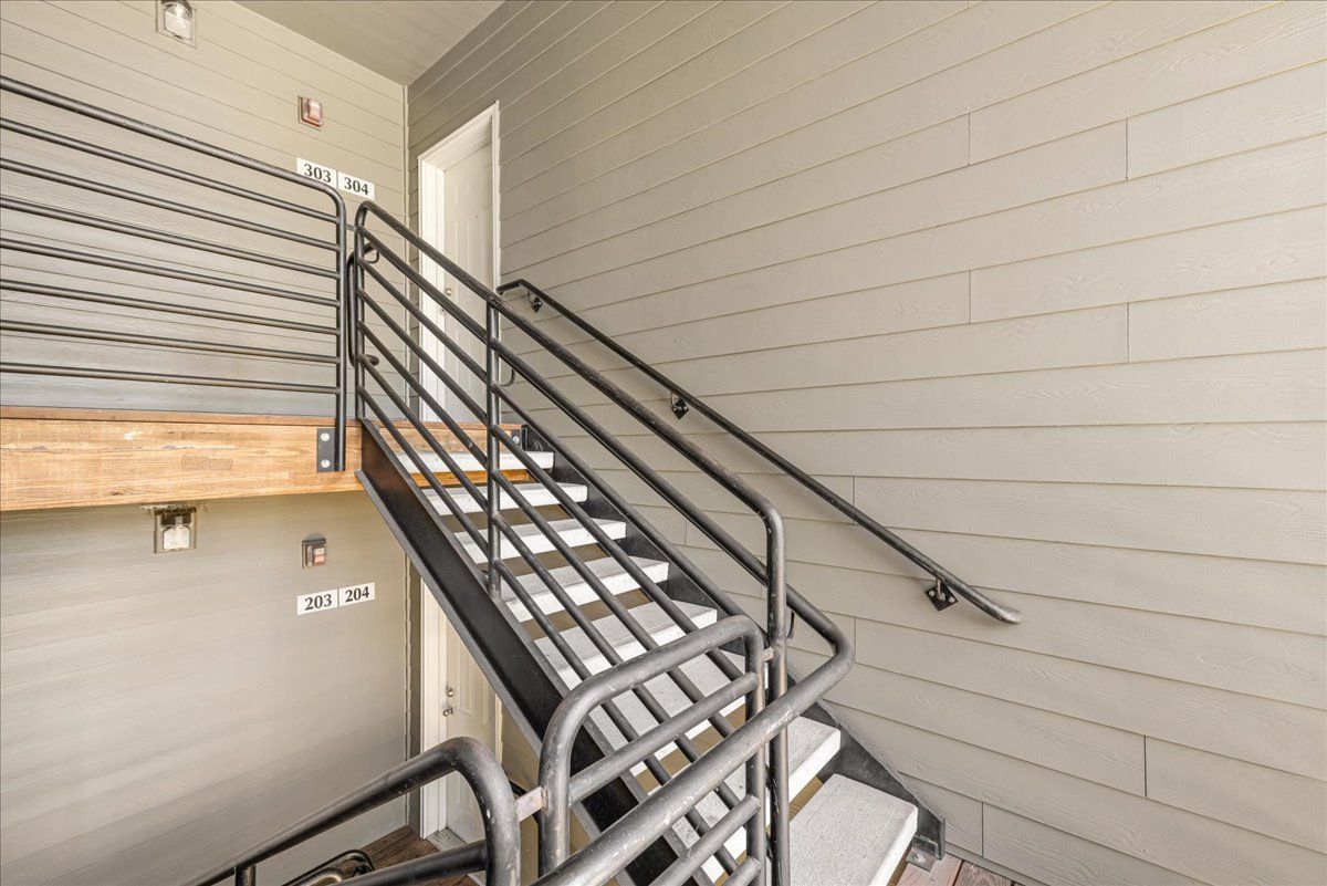 Pet-Friendly Apartments in Keizer, OR - Hawk's Point Apartments - Covered Apartment Staircase With Black Metal Railings, Numbered Entry Doors, and Gray Siding Along Shared Pathways.