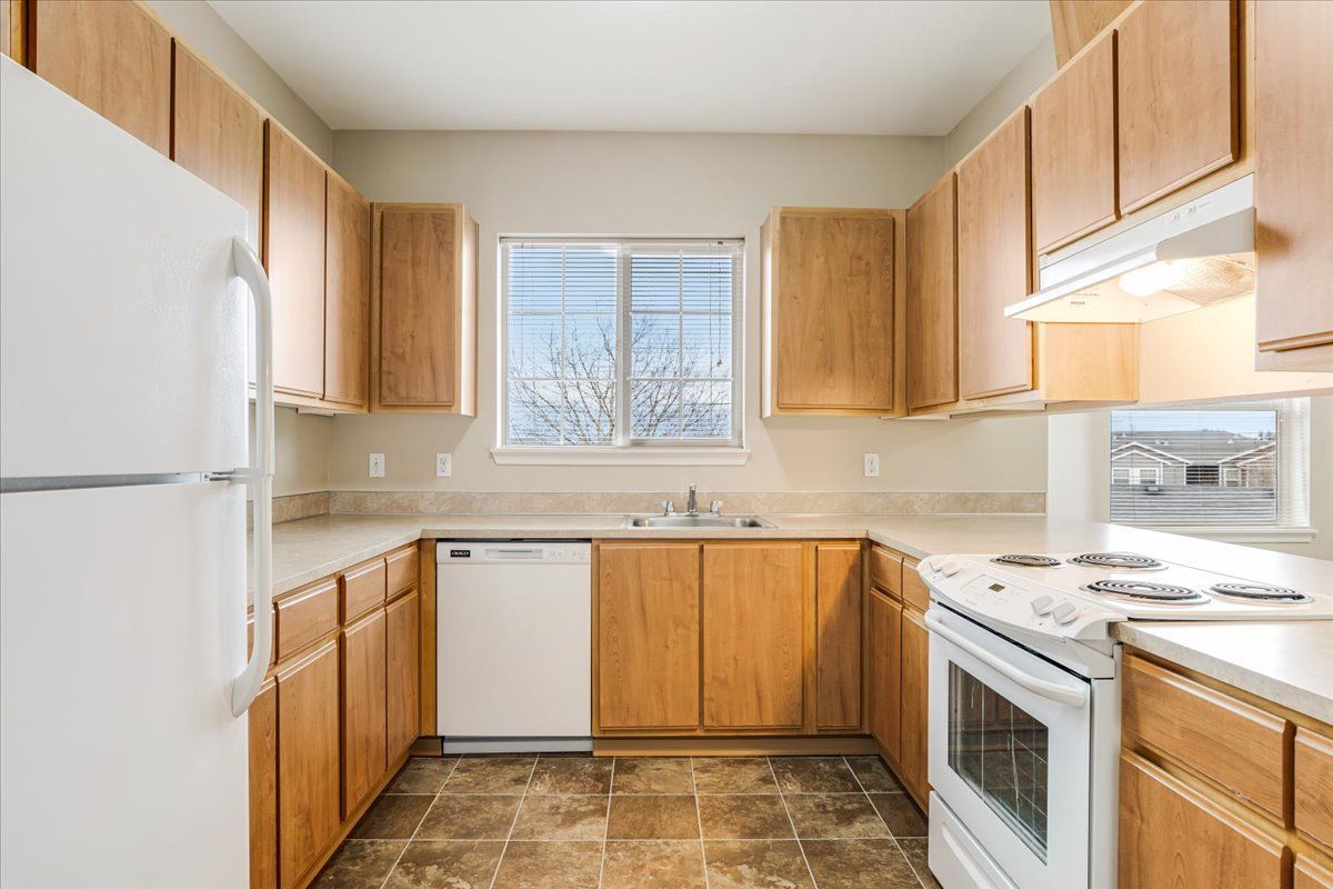 Dog-Friendly Apartments in Keizer, OR - Hawk's Point Apartments - Bright Kitchen With Natural Wood Cabinets, White Appliances, Window, and Tile Flooring.