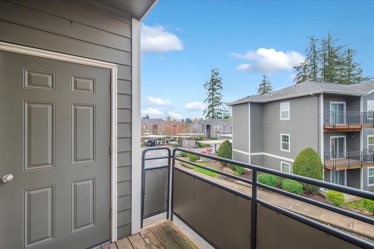 Keizer, OR, Pet-Friendly Apartments - Hawk's Point Apartments - Private Balcony With Black Railing and Gray Door, Overlooking Landscaped Grounds and Apartment Buildings.