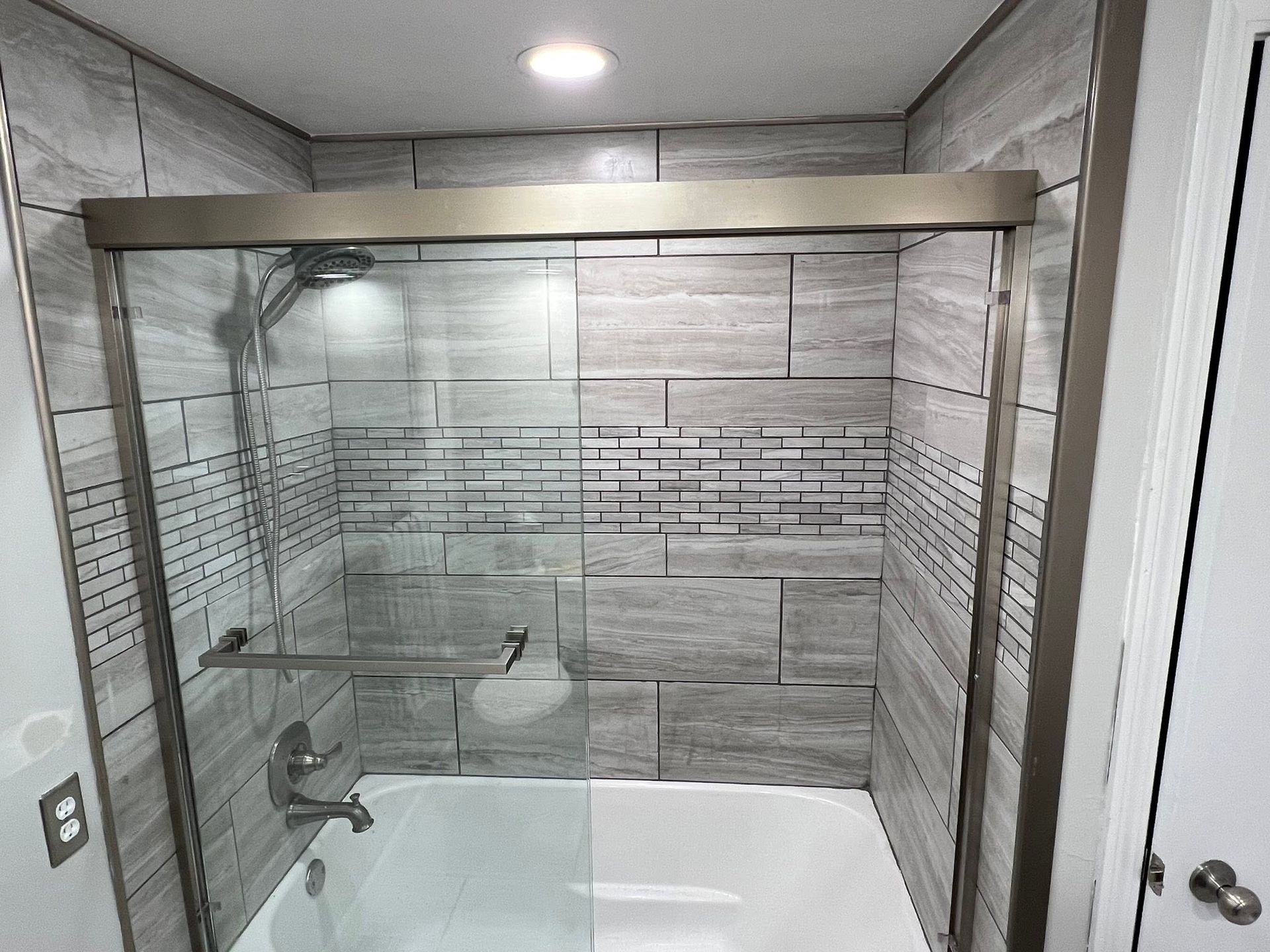 Modern bathroom with glass-enclosed tiled shower and white bathtub under recessed lights