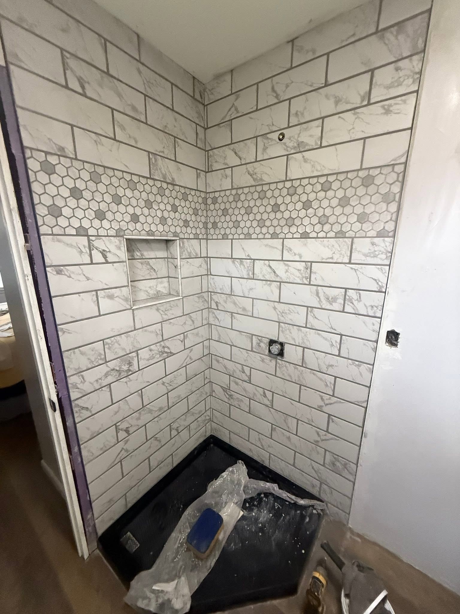 Small tiled shower stall under renovation, with a black shower pan and construction debris on the floor.