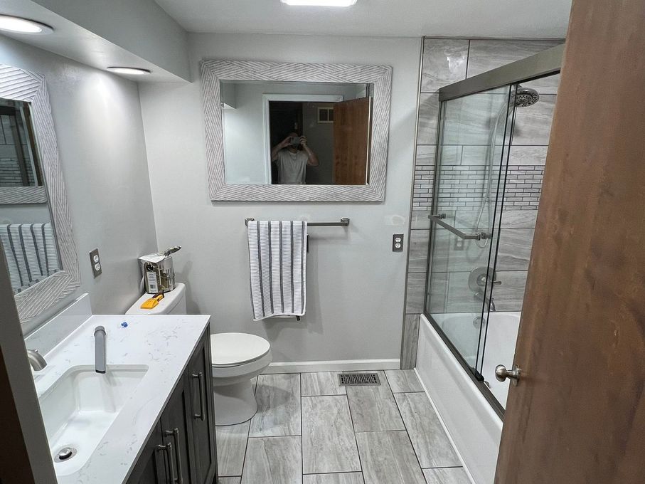 Modern bathroom with a glass shower, vanity sink, toilet, towel rack, and wood-look floor.
