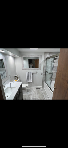 Small modern bathroom with white tiles, vanity sink, mirror, towel rack, and glass shower enclosure.
