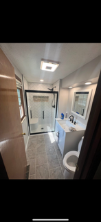 Small bathroom with glass shower, sink vanity, mirror, and toilet under bright ceiling light.