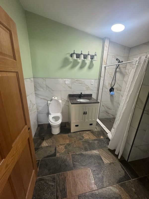 Small bathroom with toilet, sink, shower, and stone-pattern tile floor in green and white.