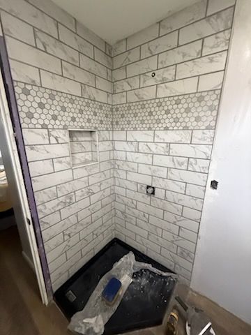 Small tiled shower stall with hex mosaic accent, black shower pan, and plumbing opening.