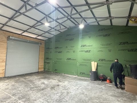 Empty warehouse interior with roll-up door, green insulated wall, and one person standing near tools