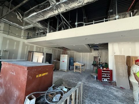 Construction site interior with exposed ducts, drywall, tools, and a large red dumpster