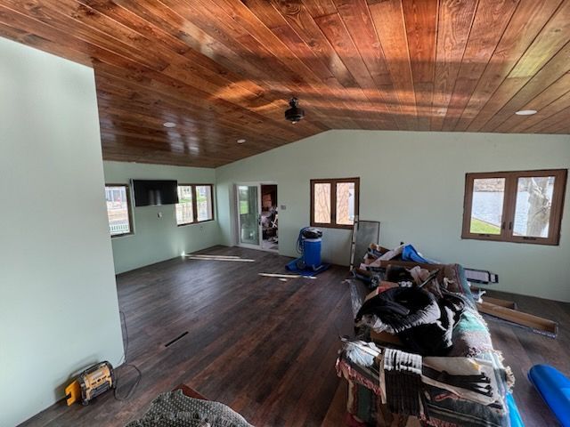 Empty room with wood ceiling, dark floor, windows, and a few stacked items on the right