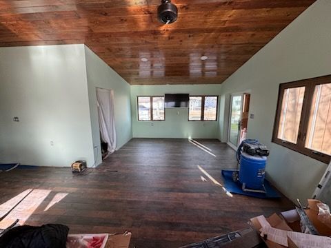 Empty room with dark wood ceiling, light green walls, windows, and a blue cleaning machine
