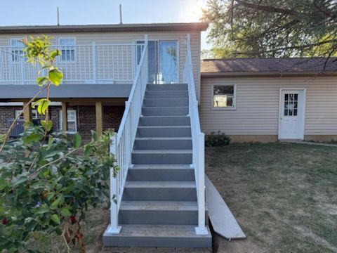Front yard staircase with white railings leading to an elevated deck beside a beige house.