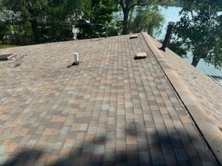 Rooftop with brown shingles, vents, and trees and water visible beyond the edge