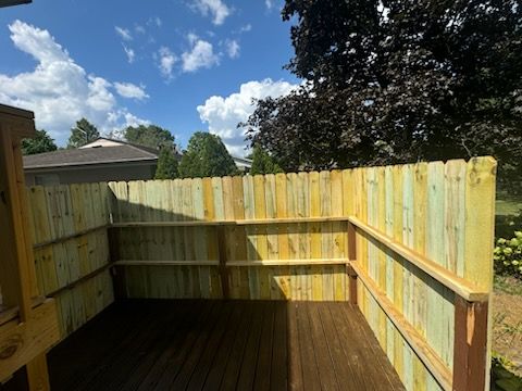 Wooden fenced backyard deck with built-in bench seating under a partly cloudy blue sky