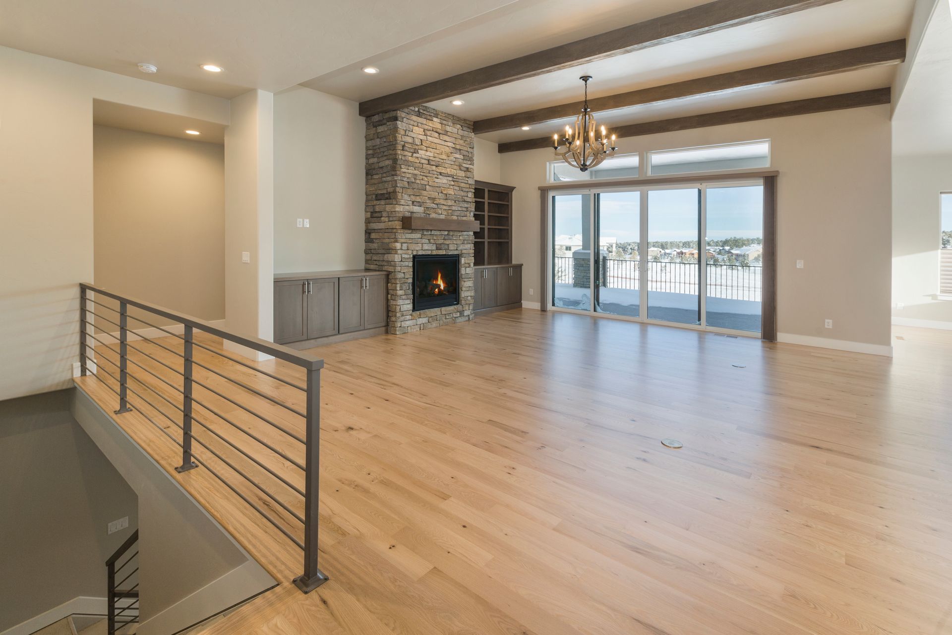 Modern open-concept living room with stone fireplace, wood floors, and balcony view