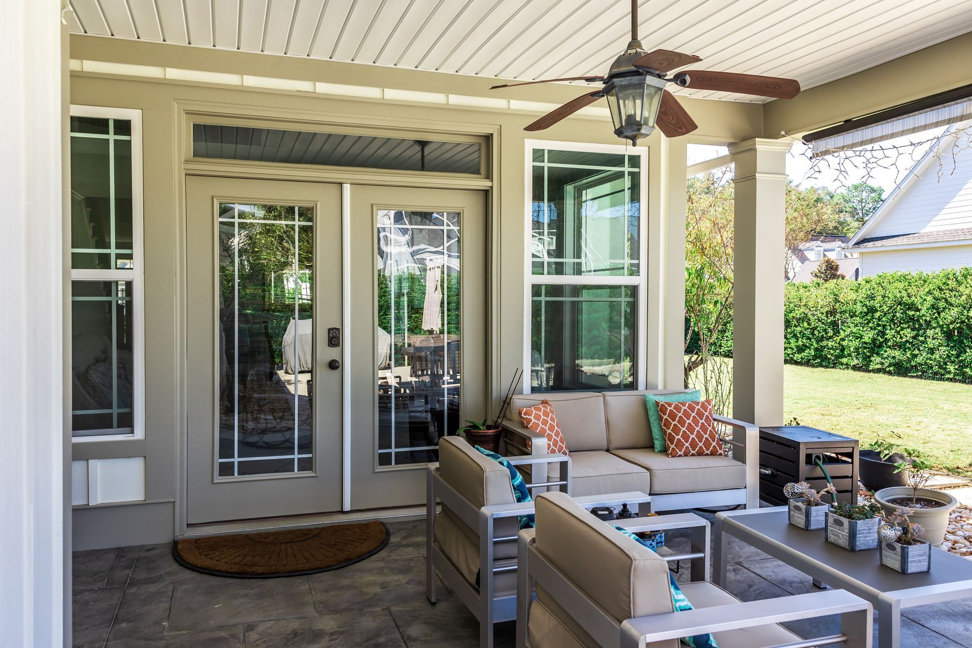 Covered patio with white outdoor seating, ceiling fan, and glass French doors leading inside.
