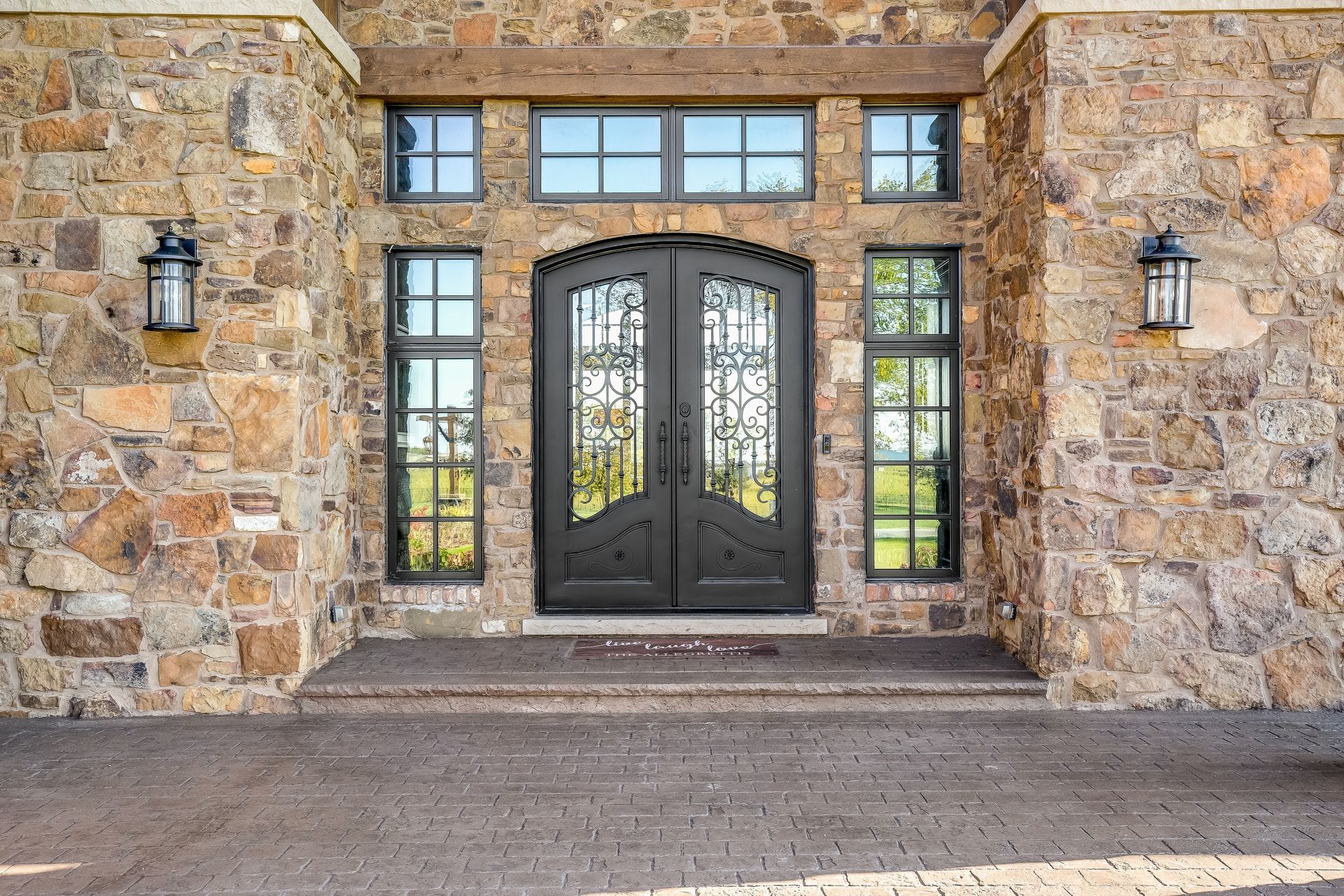 Stone entrance with black double doors, sidelights, and lanterns on a rustic exterior wall