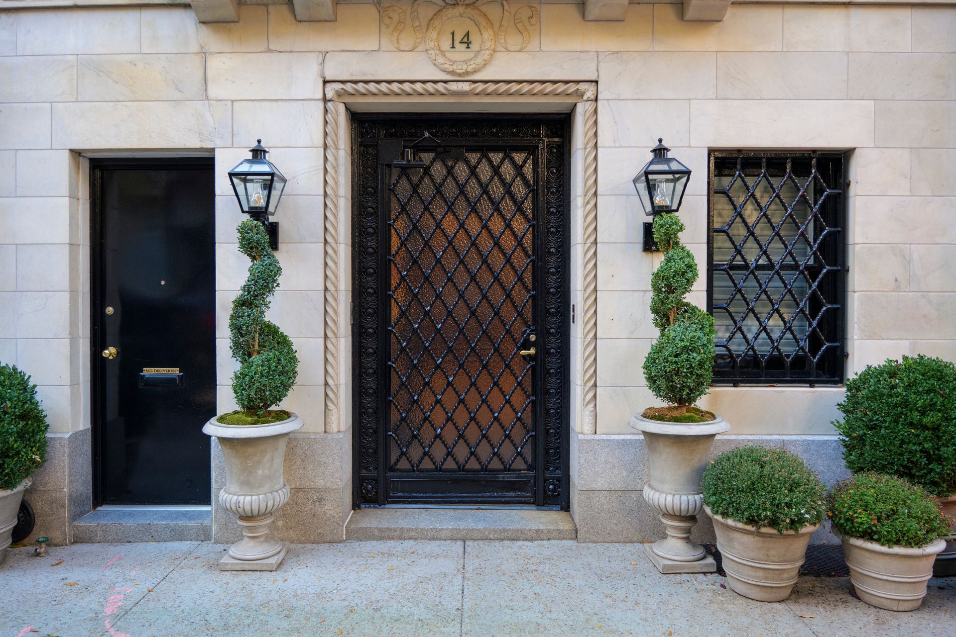 Elegant stone townhouse entrance with black iron door, lanterns, potted shrubs, and topiary decorations