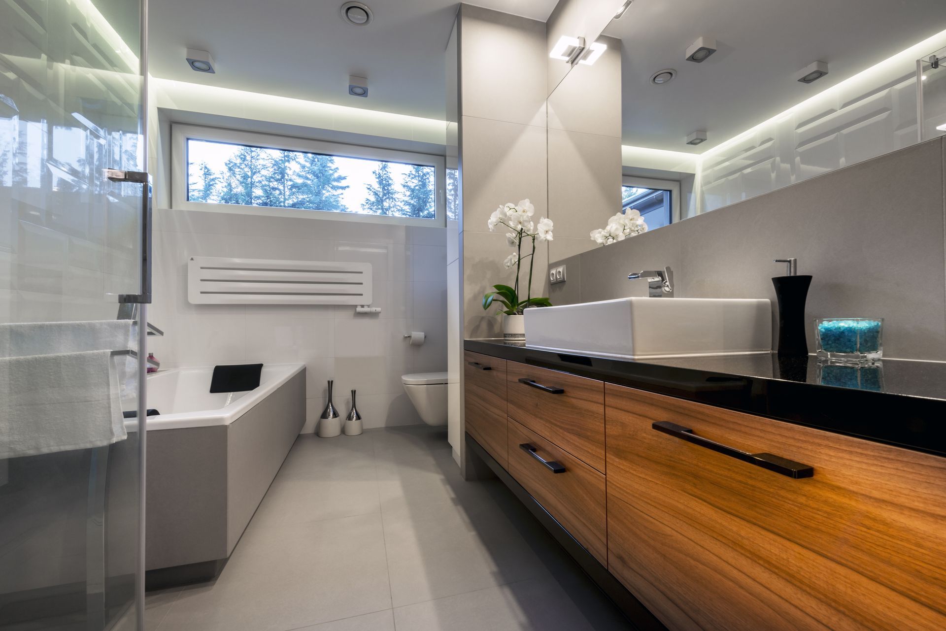 Modern bathroom with a black countertop vanity, wood drawers, bathtub, and window with snowy trees outside