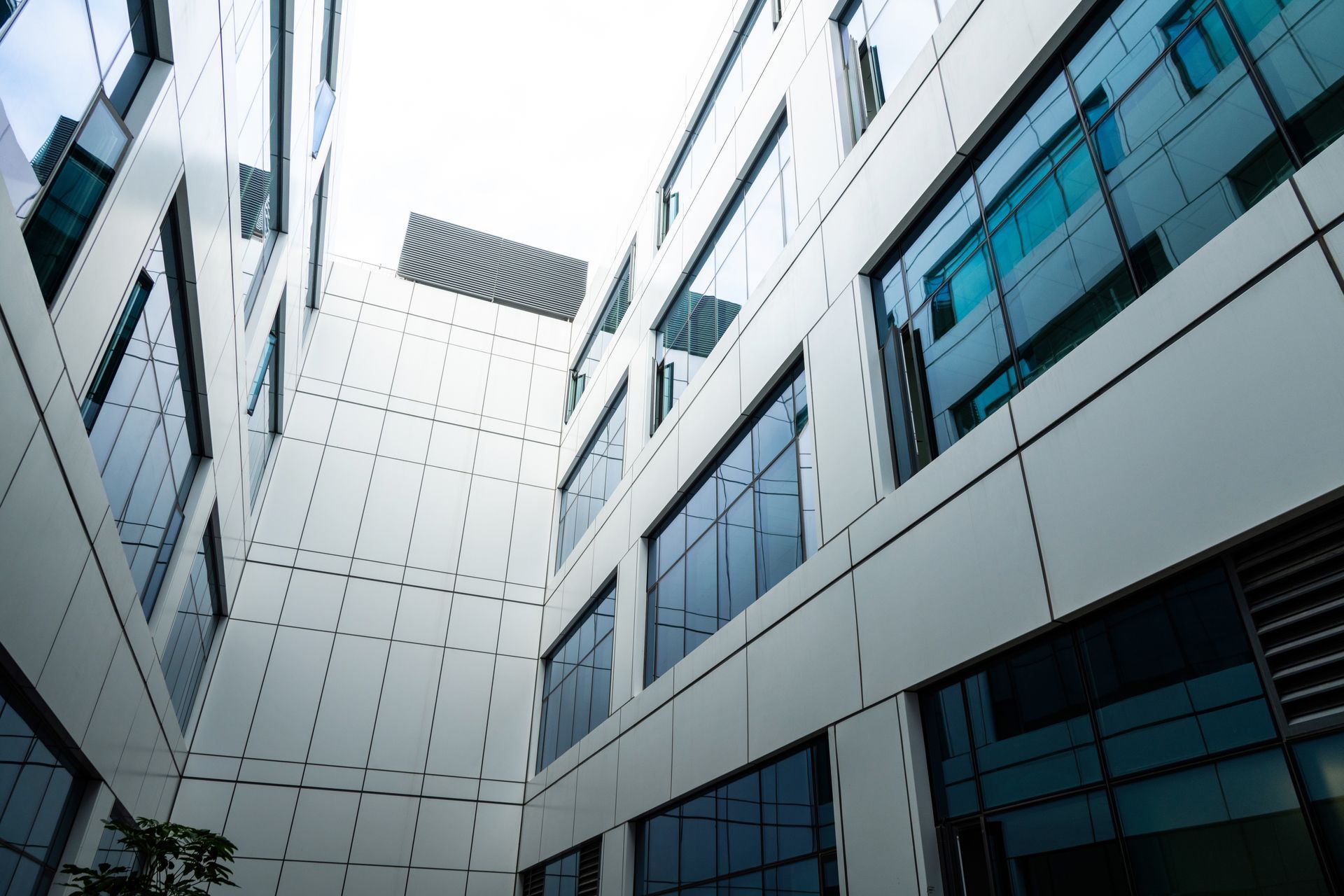Modern office courtyard between white buildings with blue-tinted windows, viewed from below
