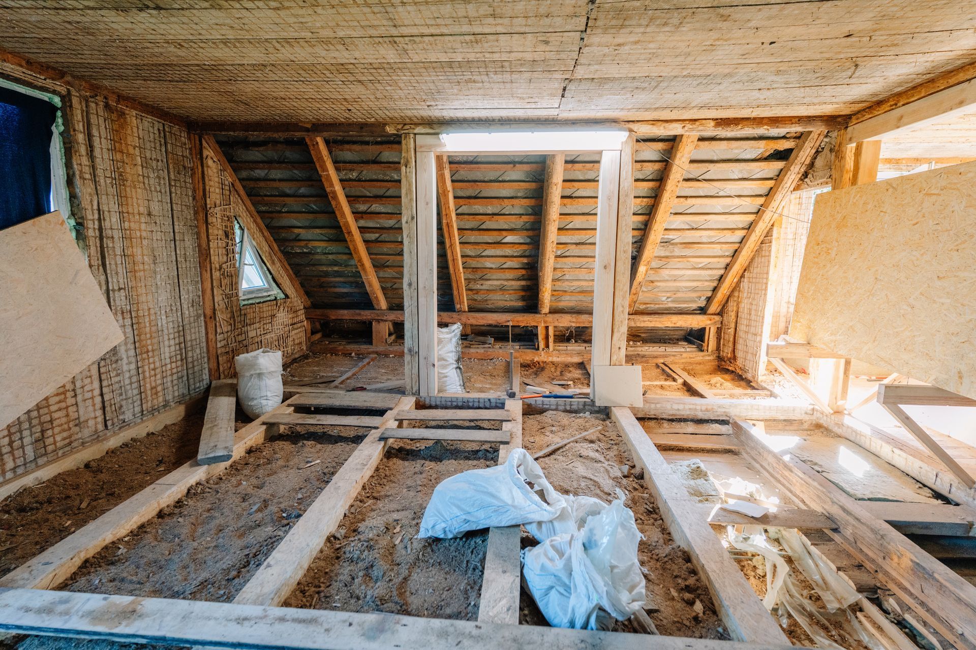 Unfinished attic with exposed wooden beams, floor joists, and insulation materials scattered around