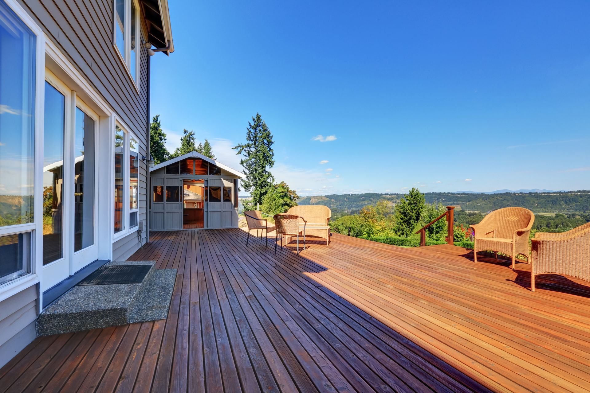 Wooden deck with two chairs, lakeside view, and a house under a clear blue sky