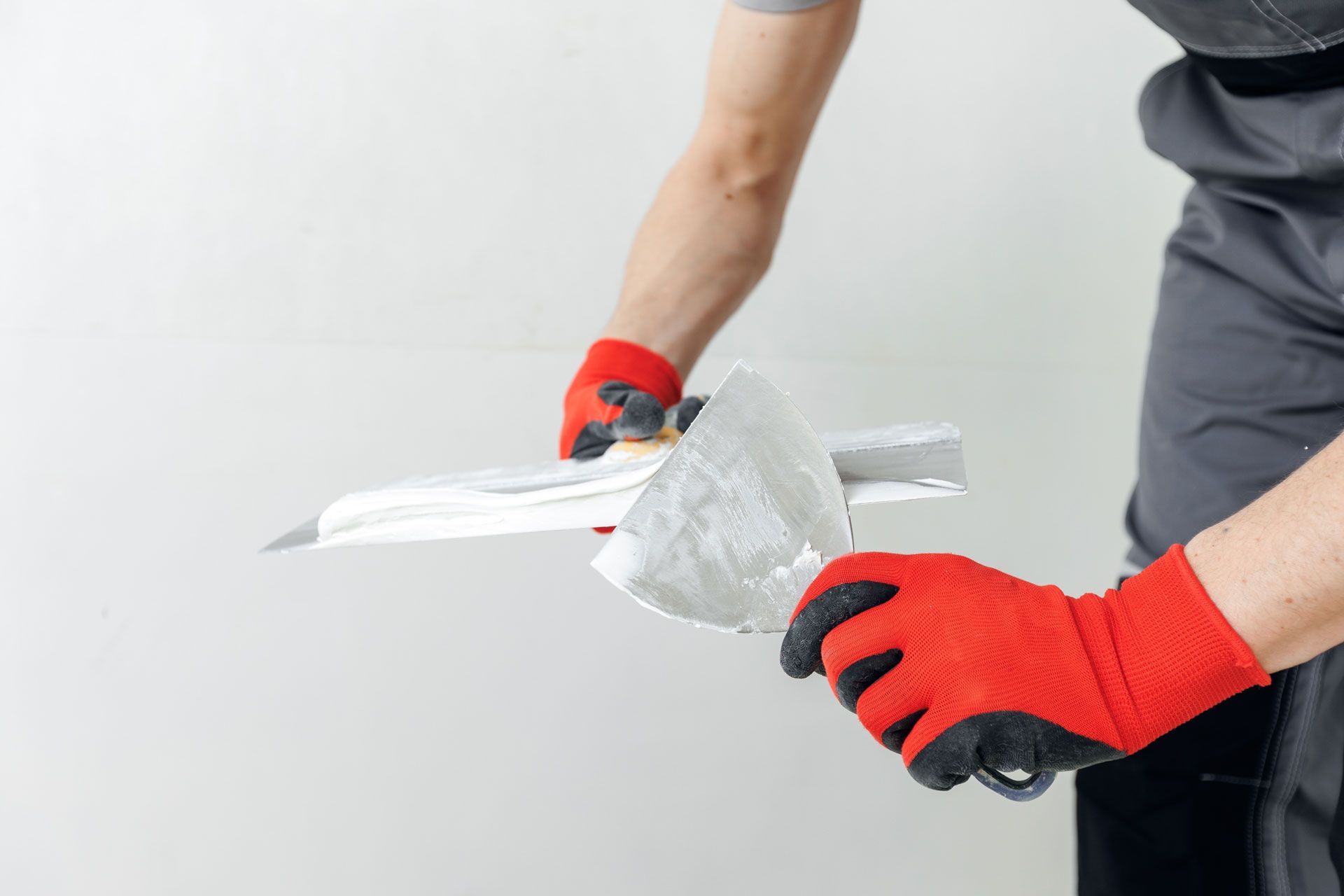 Close-up of gloved hands applying silver duct tape to a white wall with a putty knife