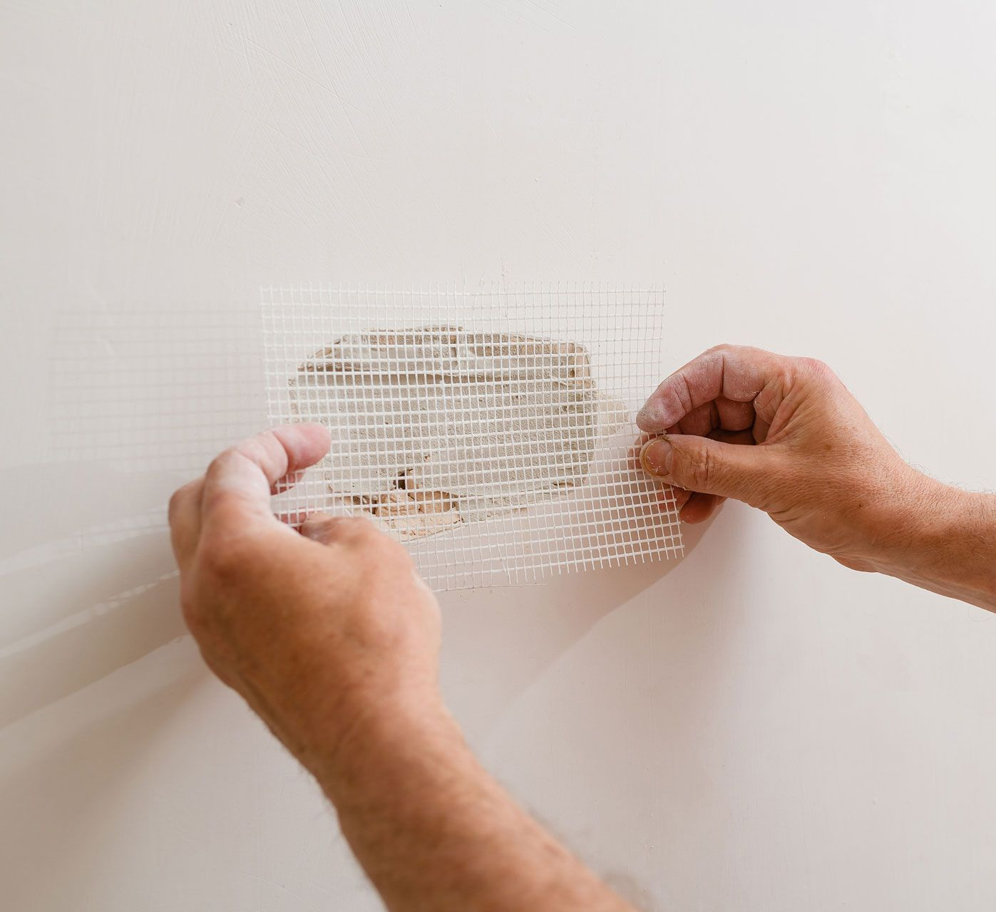 Hands applying a small patch to a white wall