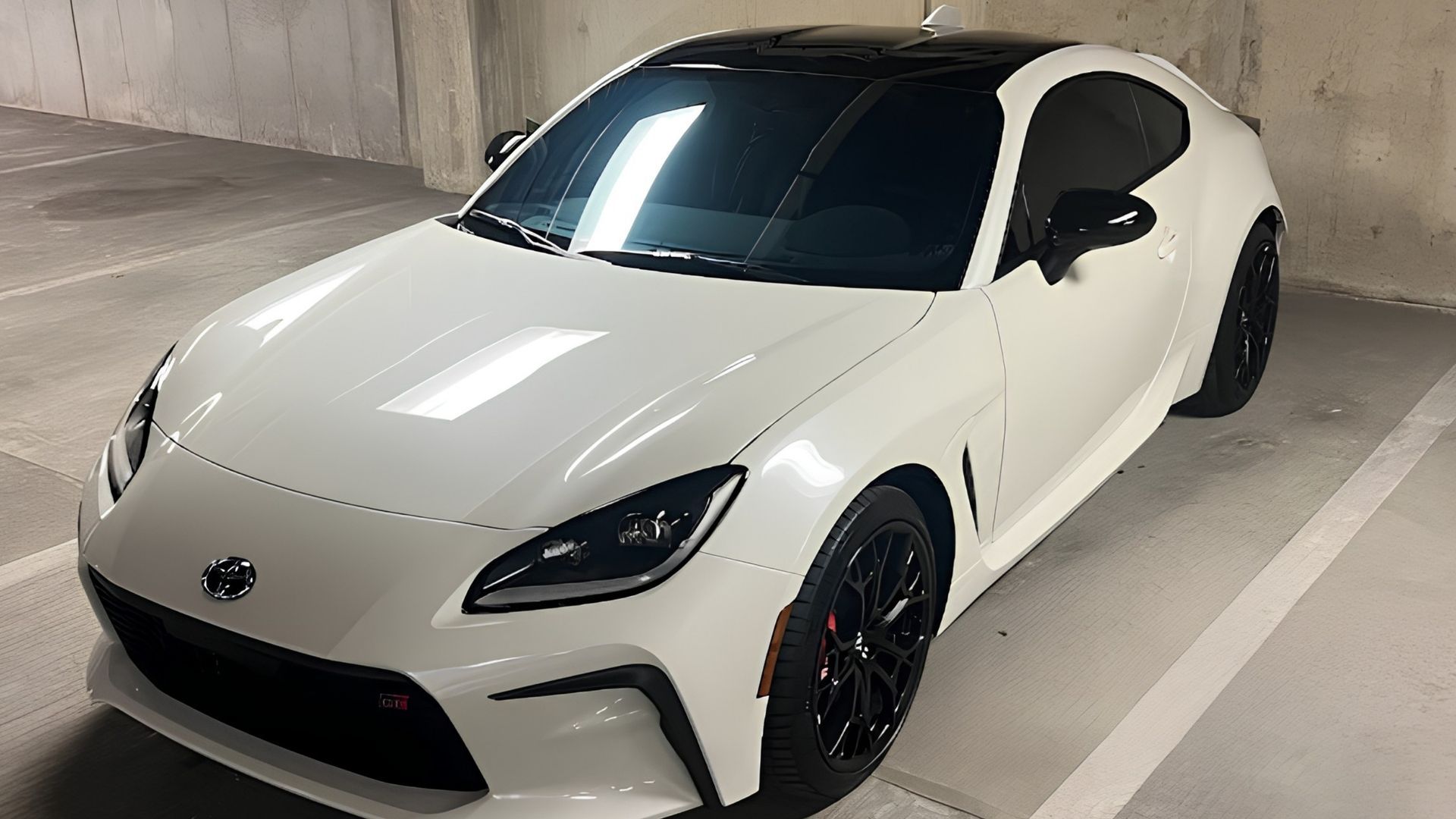 White sports coupe parked in a garage, shown from the front-left angle with black wheels and tinted windows
