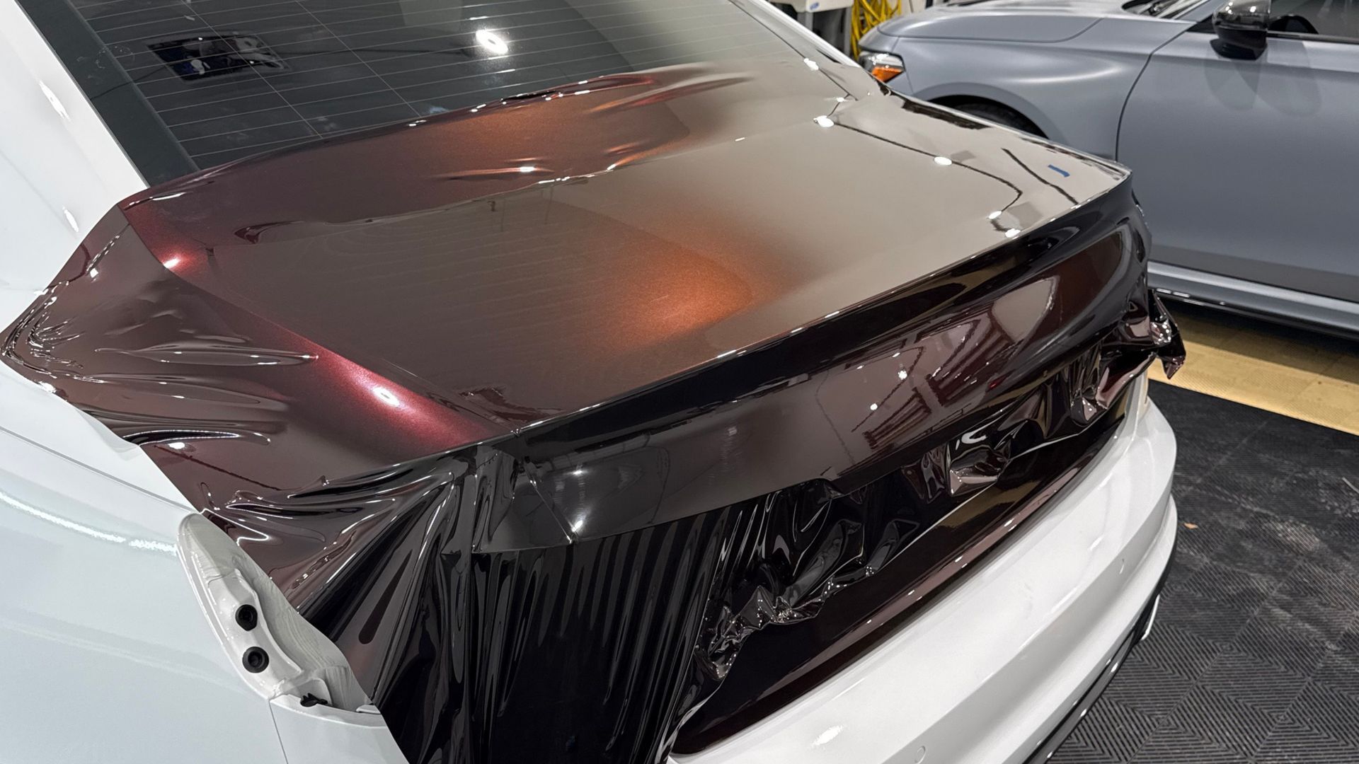Damaged black car rear panel with deep dents and creases in a parking garage