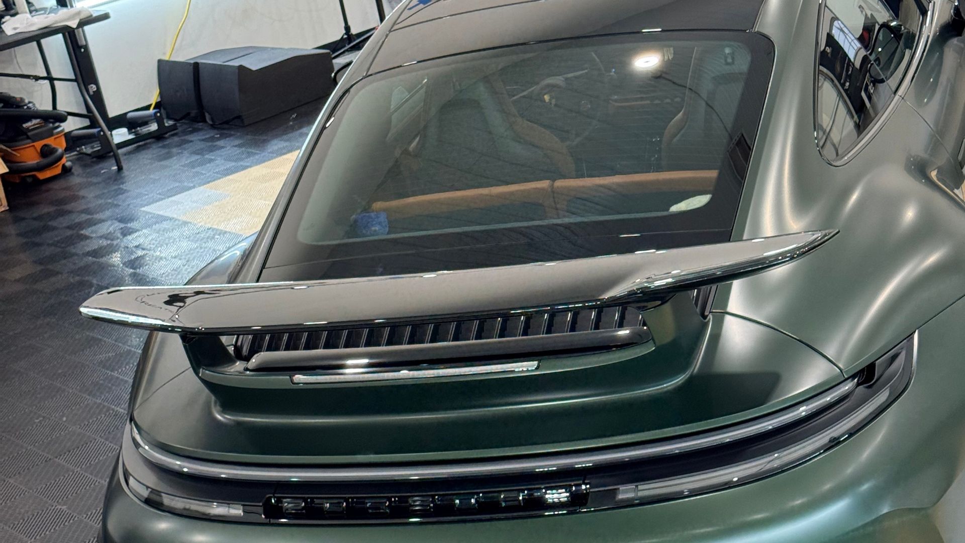 Green sports car in a garage with its rear wing and taillights visible