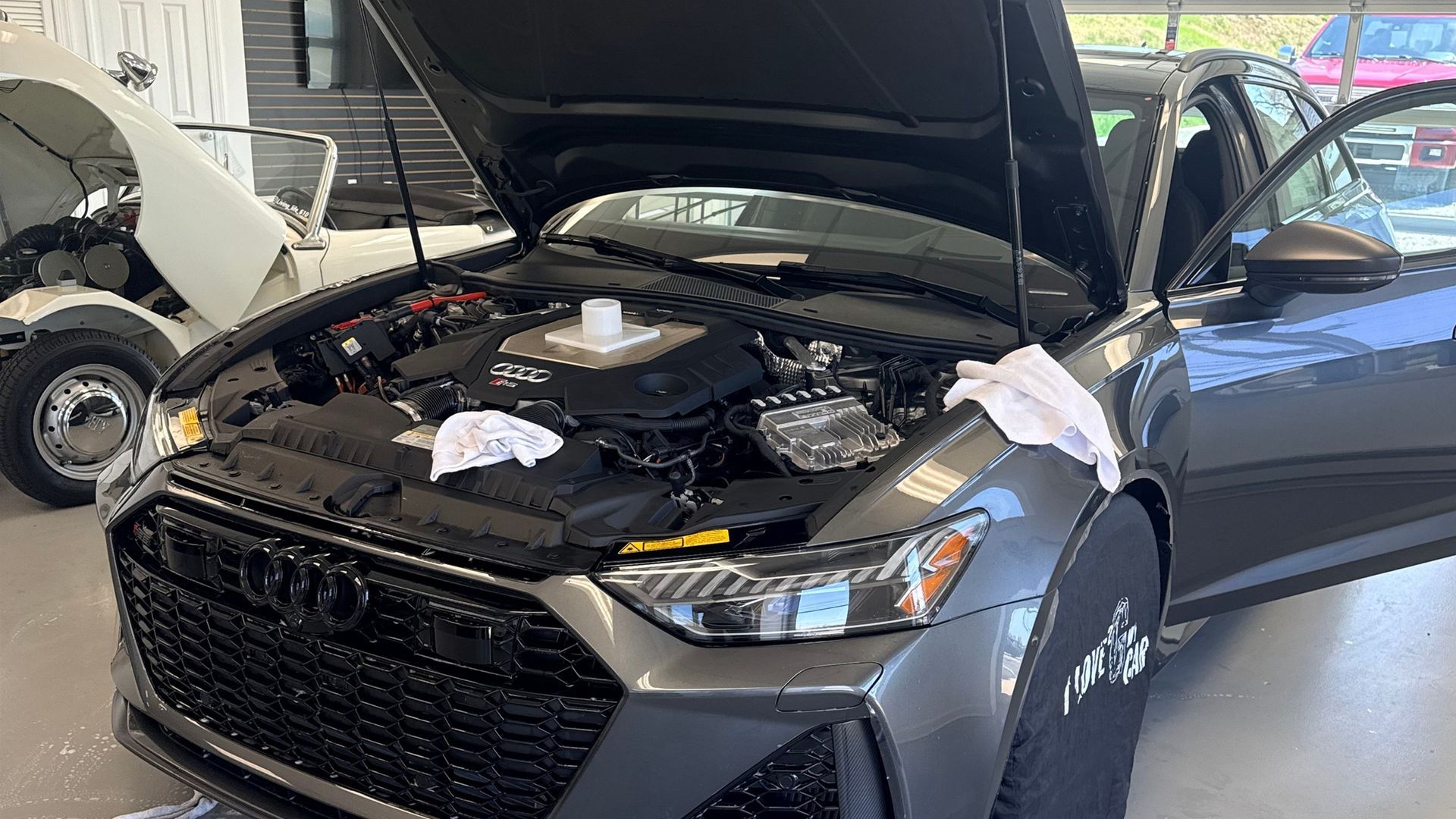 Black sedan with hood open in a garage, exposing the engine compartment.