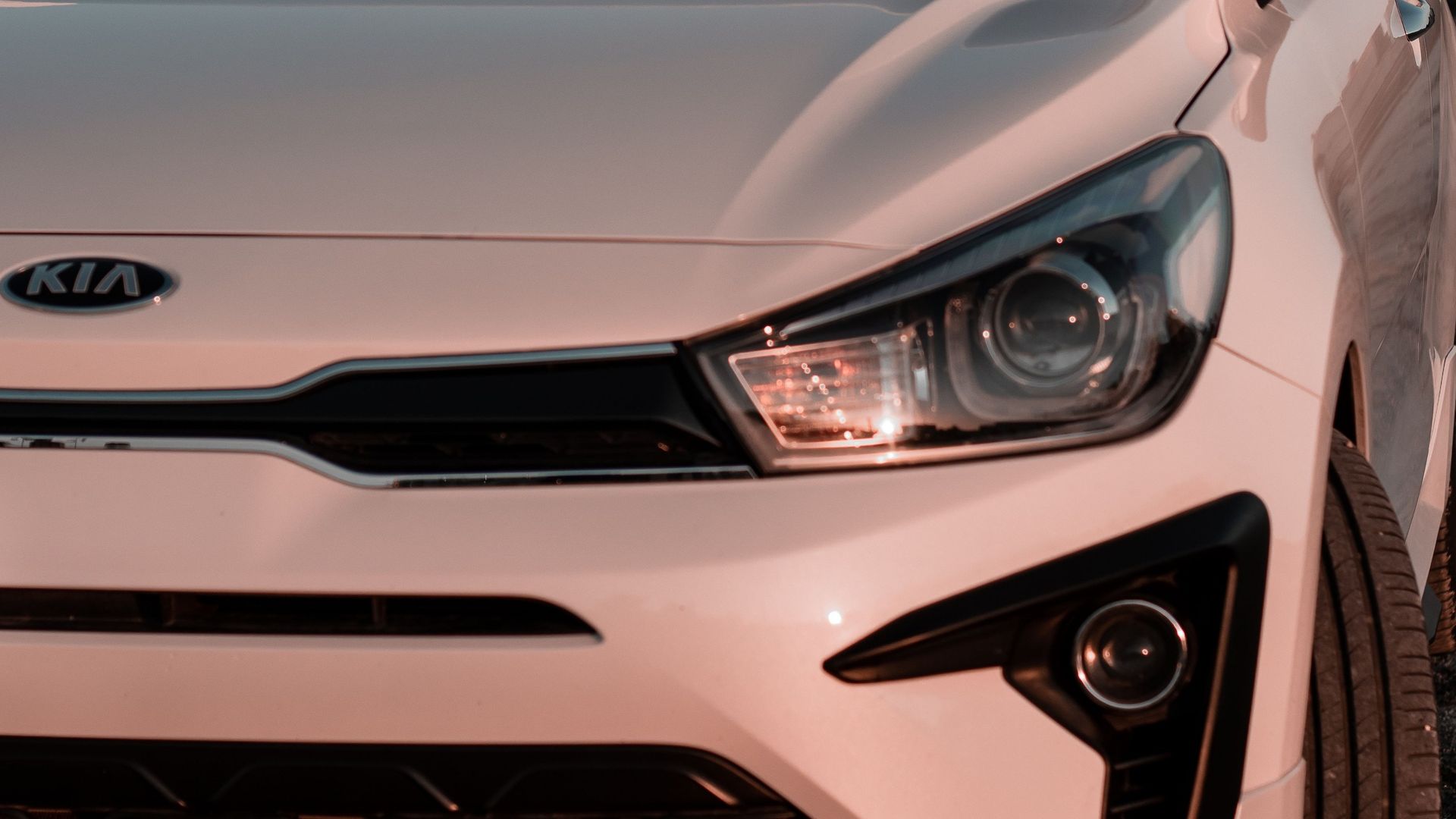Close-up of a white Kia car’s front end with headlight and grille visible