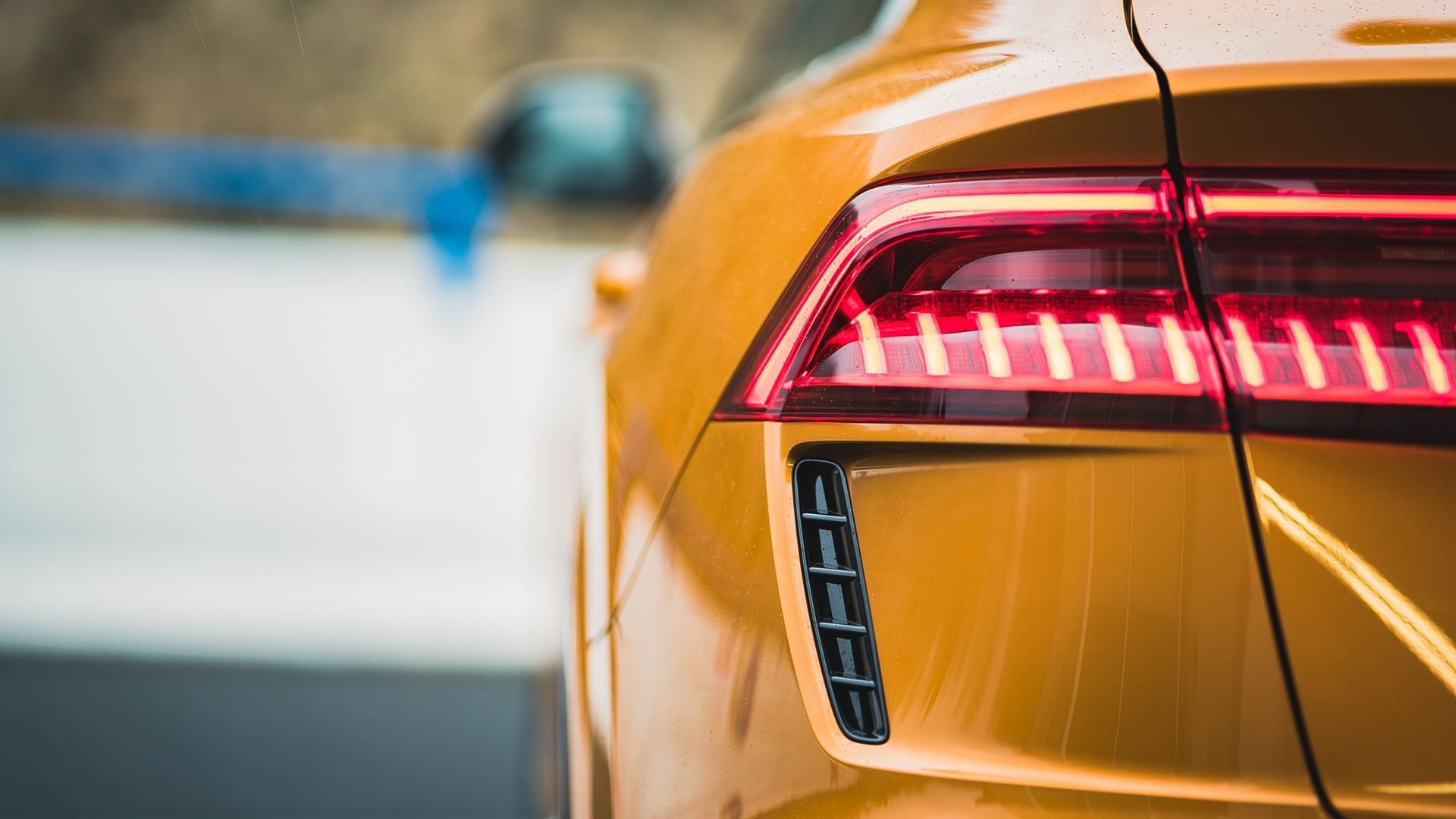 Close-up of a yellow car’s rear with a glowing red taillight and blurred road background