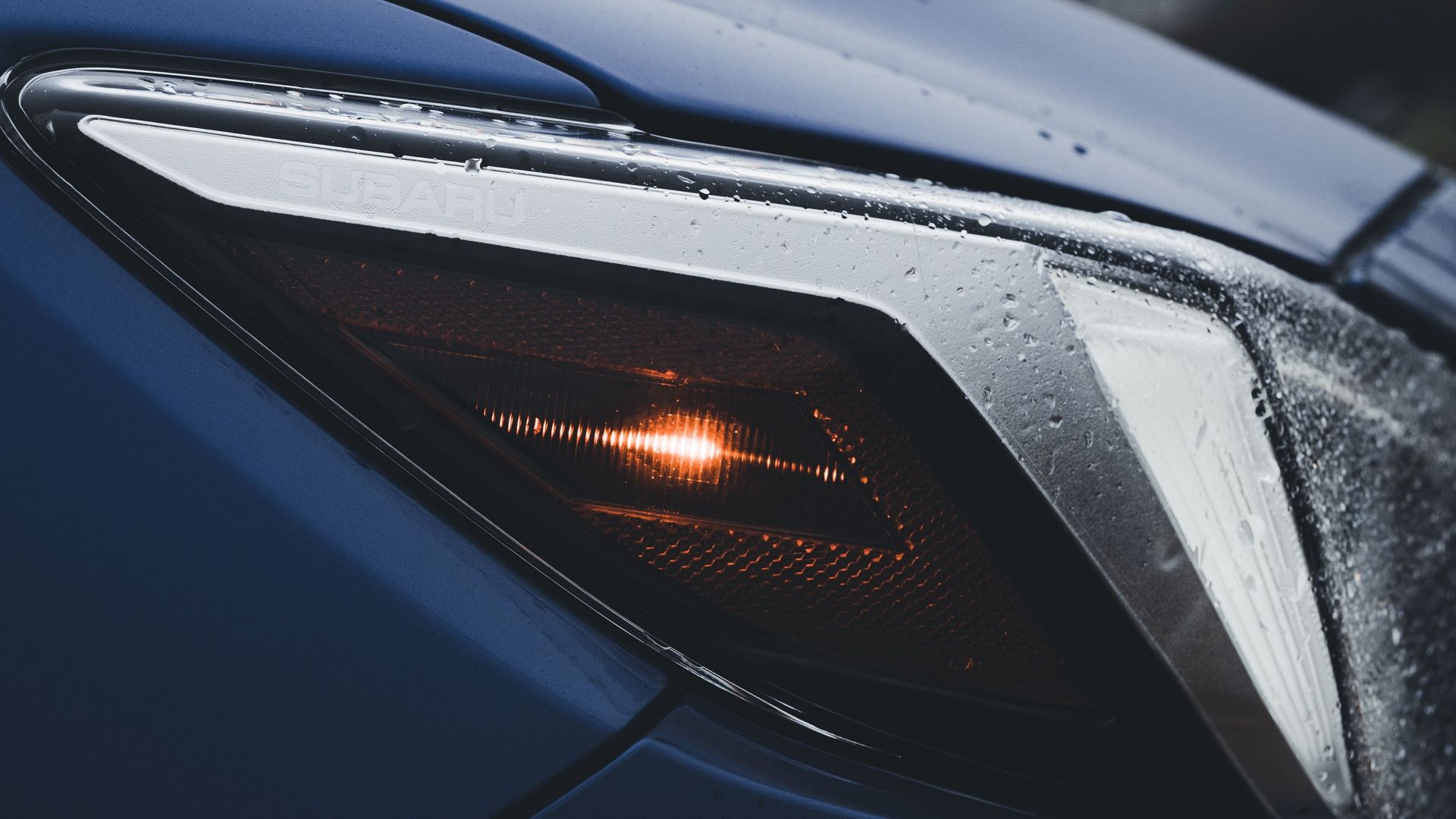 Close-up of a blue car’s front headlight with an orange indicator light on.