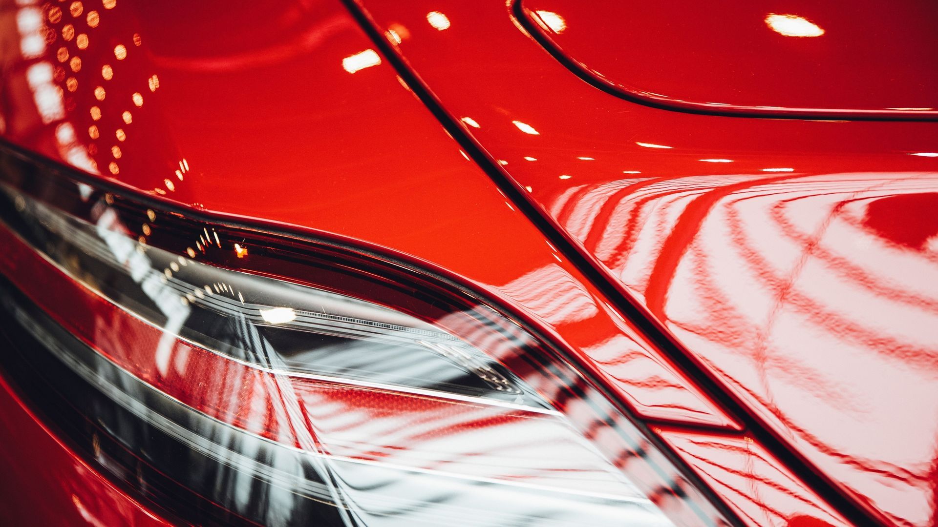 Close-up of a glossy red car’s rear taillight and body panel with white reflections