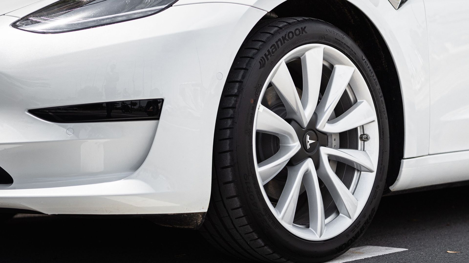Close-up of a white car’s front wheel and bumper on a road