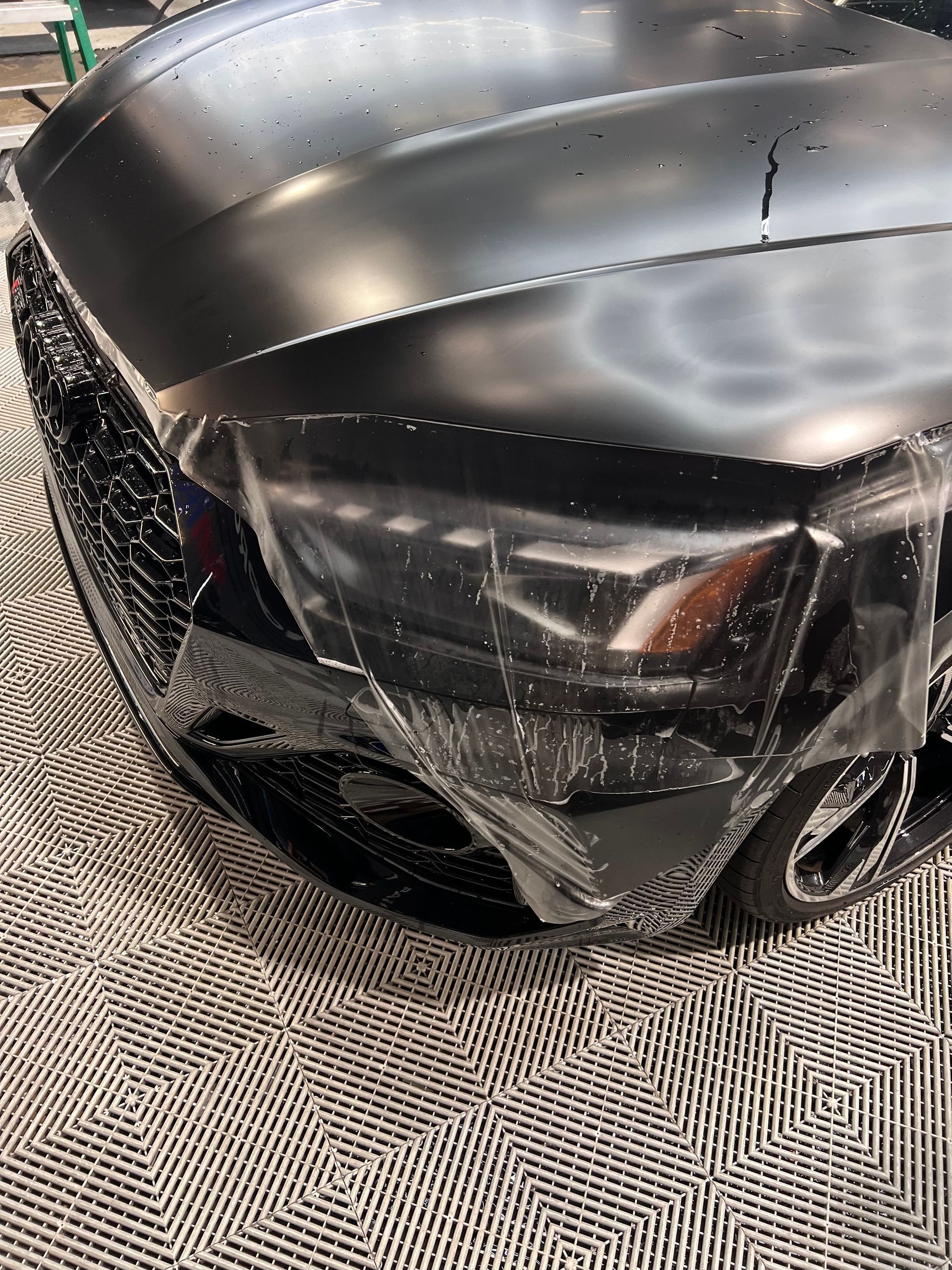 A black car is wrapped in plastic and sitting on a carpet.