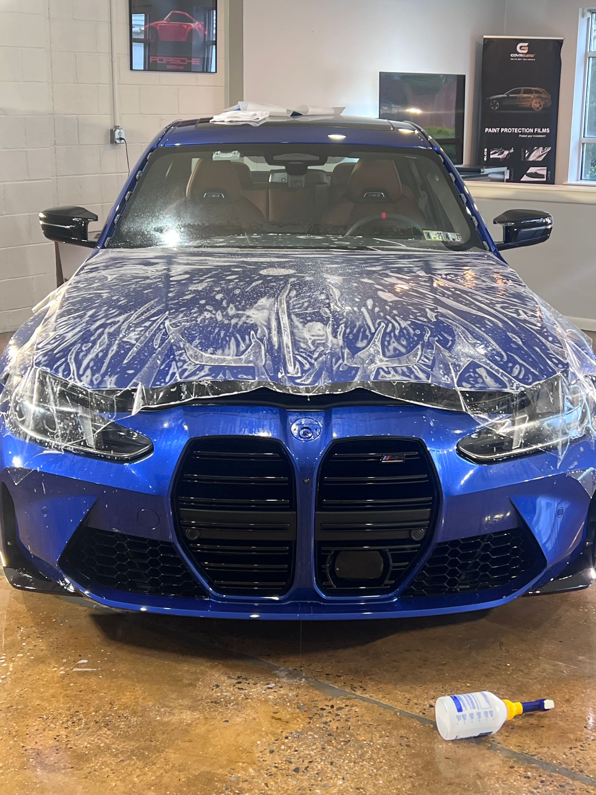 A blue bmw is covered in plastic wrap in a garage.