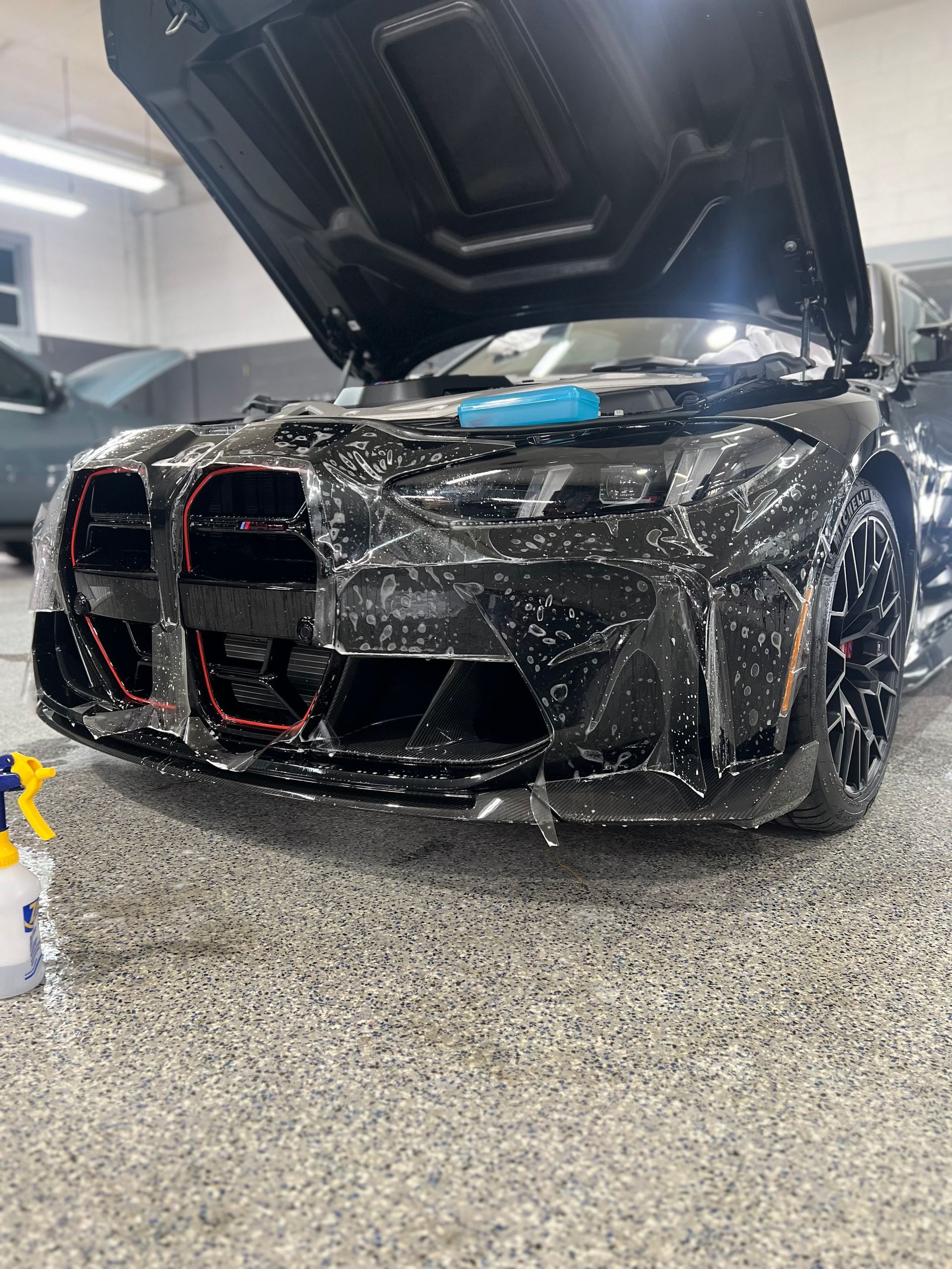 A black car is covered in plastic wrap in a garage.